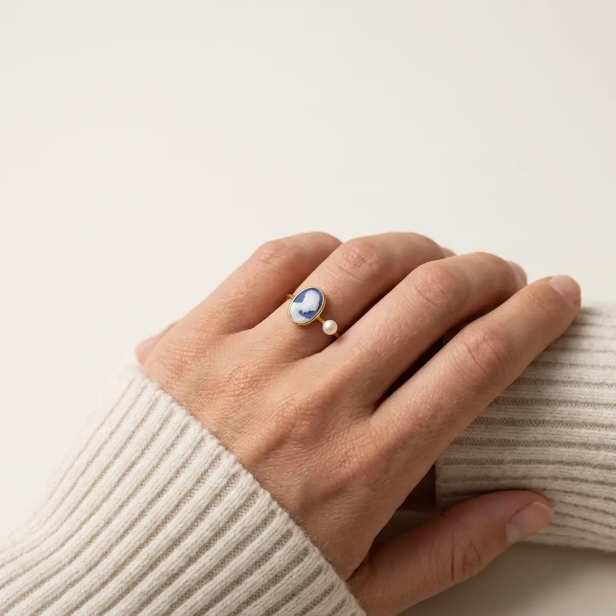 Bague camée bleue ornée d'une perle et portée avec les mains croisées